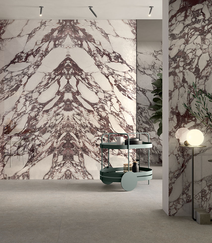 Ambiente contemporaneo con grandi superfici effetto marmo dalle venature bordeaux, abbinate a pavimento neutro e arredi di design.