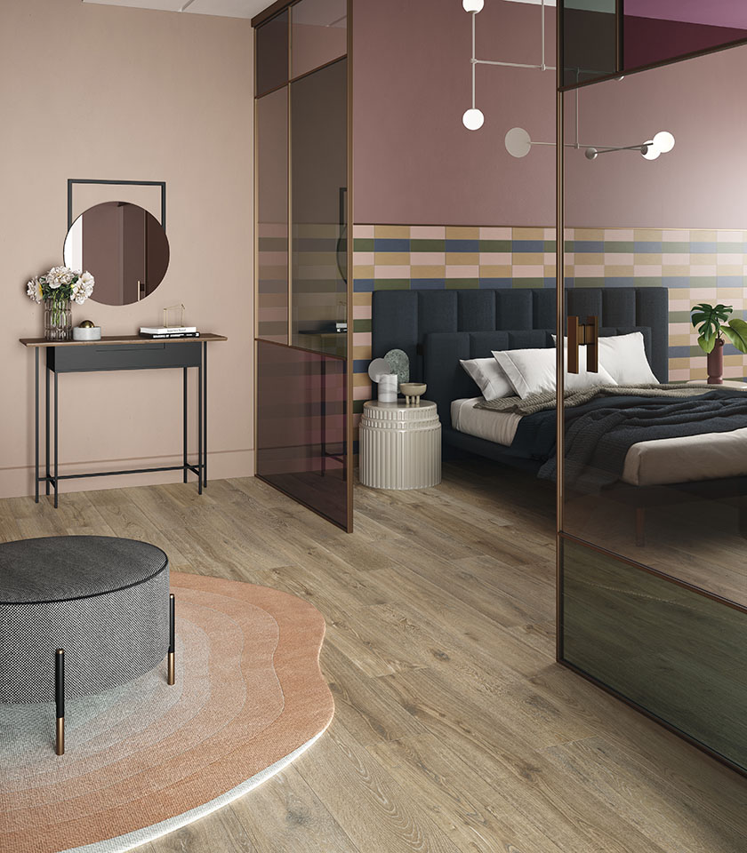 Bio Attitude Barrel porta nella camera da letto il calore del legno ceramico, in dialogo con le tonalità delicate di Pigmenti per un ambiente accogliente e contemporaneo.