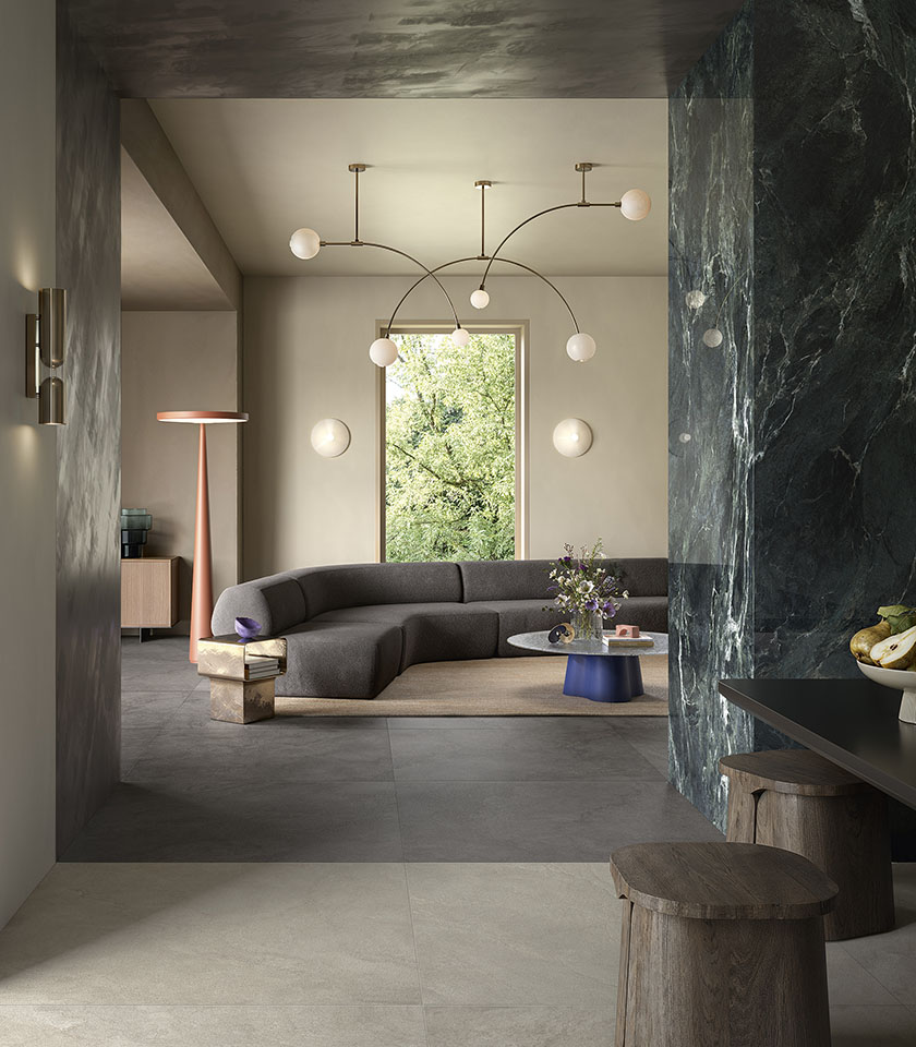Pulse Clay e Shadow definiscono un living sofisticato e materico, dove superfici ceramiche effetto pietra dialogano con l’intensità decorativa di Noblesse Verde Alpi.