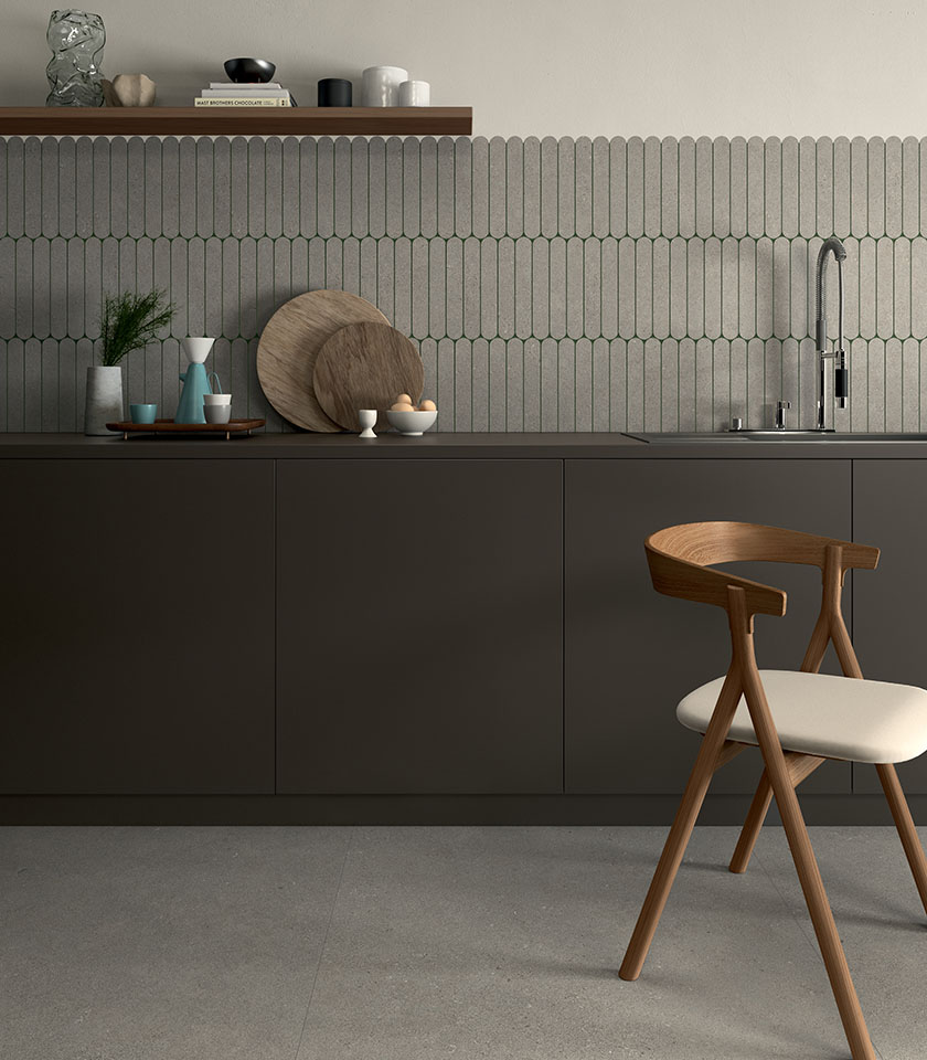 Cucina minimal chic con pavimento effetto cemento, rivestimento geometrico tono su tono, mobili scuri e dettagli in legno dal design essenziale.
