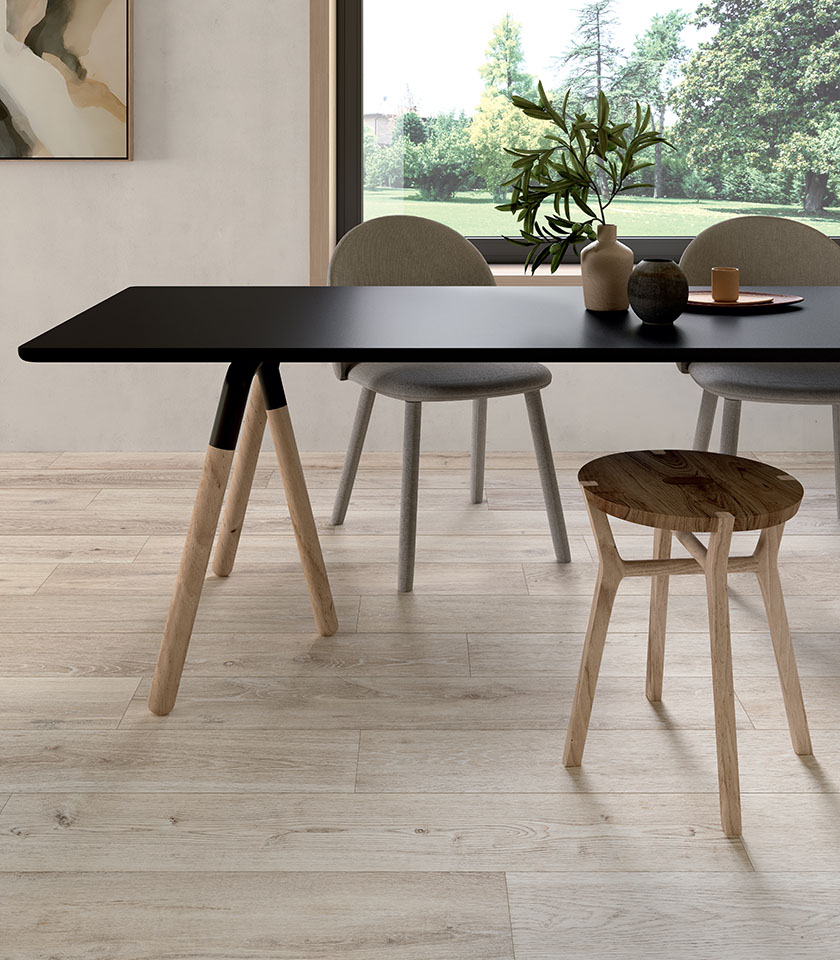 Zona pranzo contemporanea con tavolo nero e sedute in legno, su pavimento della collezione Bio Attitude effetto legno nella tonalità Cotton.