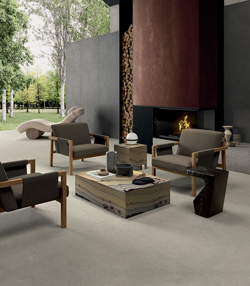 Zona living contemporanea con camino e affaccio sul verde, pavimento della collezione Intense effetto pietra nella tonalità Perle e rivestimento della collezione Pigmenti nella tonalità Basalt.