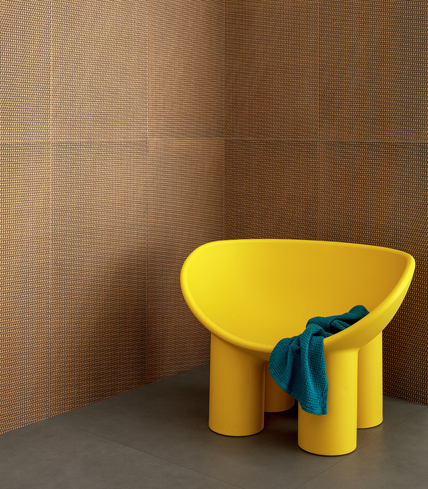 Interno bagno contemporaneo con rivestimento decorativo nei toni arancio e nero, poltrona gialla e dettagli tessili blu.