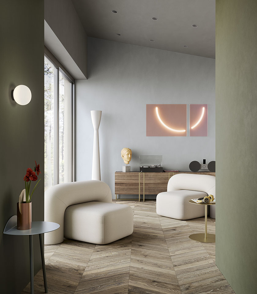 Soggiorno contemporaneo con pavimento effetto legno a spina, pareti verde salvia, poltrone bianche e dettagli di design.