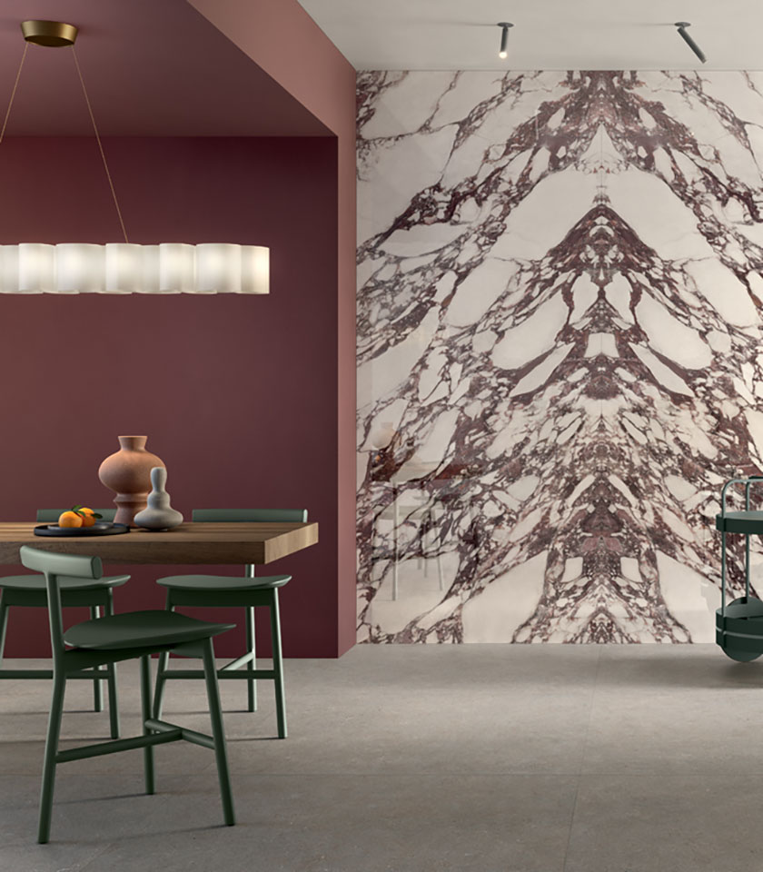 Sala da pranzo contemporanea con parete decorativa effetto marmo, tonalità bordeaux, tavolo in legno e sedie verdi.