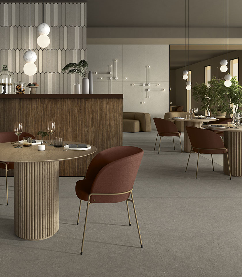 Ristorante contemporaneo con pavimento grigio effetto pietra, tavoli scultorei, sedute bordeaux e dettagli in legno.