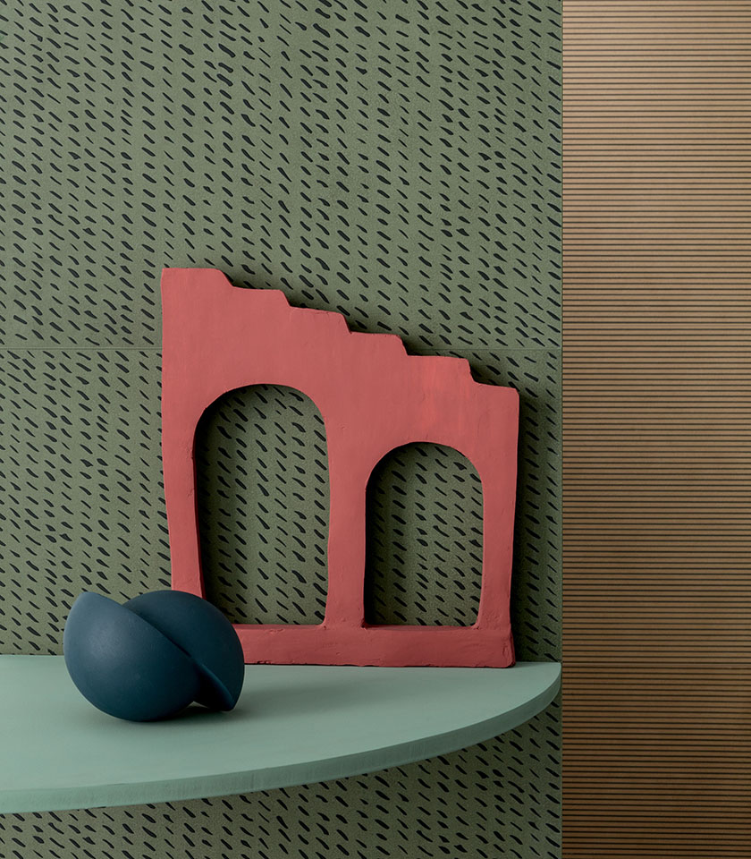 Dettaglio decorativo con rivestimento verde a motivo grafico, elemento scultoreo rosso e mensola dalle tonalità naturali.
