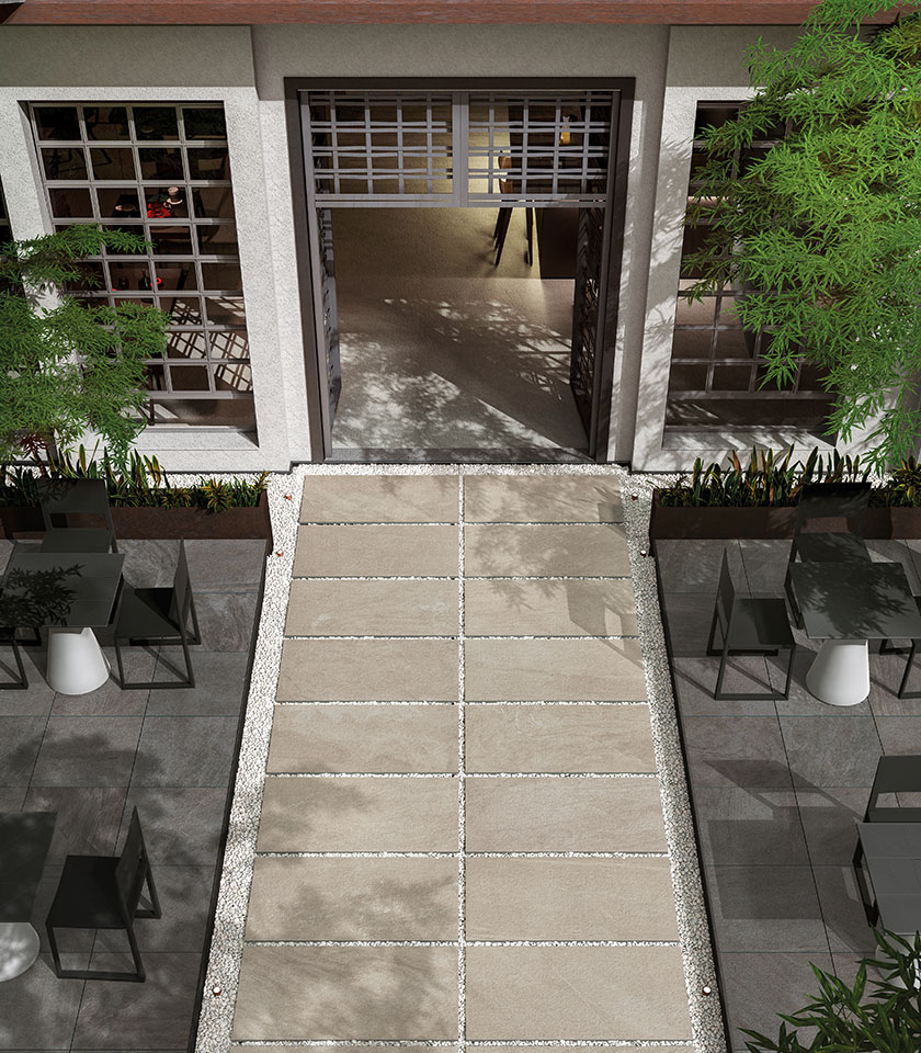 Spazio outdoor contemporaneo con pavimentazione in gres porcellanato effetto pietra, grandi lastre posate su ghiaia, arredi essenziali e vegetazione integrata.