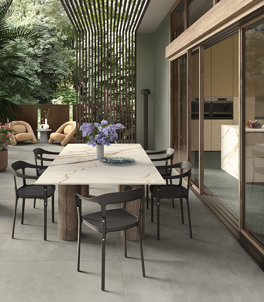 Terrazza contemporanea con pavimento in gres porcellanato, arredi di design, grande tavolo effetto marmo e continuità tra spazi interni ed esterni.
