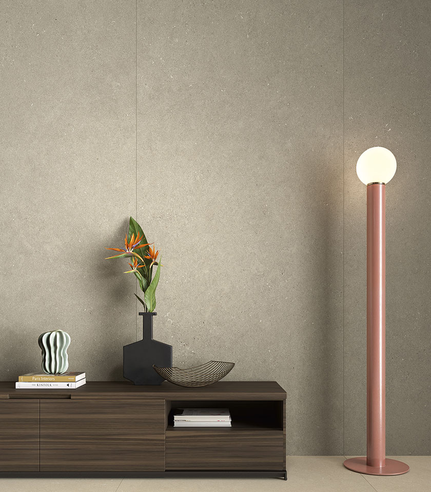 Interno contemporaneo con rivestimento a parete in grandi lastre effetto cemento, mobile basso in legno e lampada da terra decorativa.
