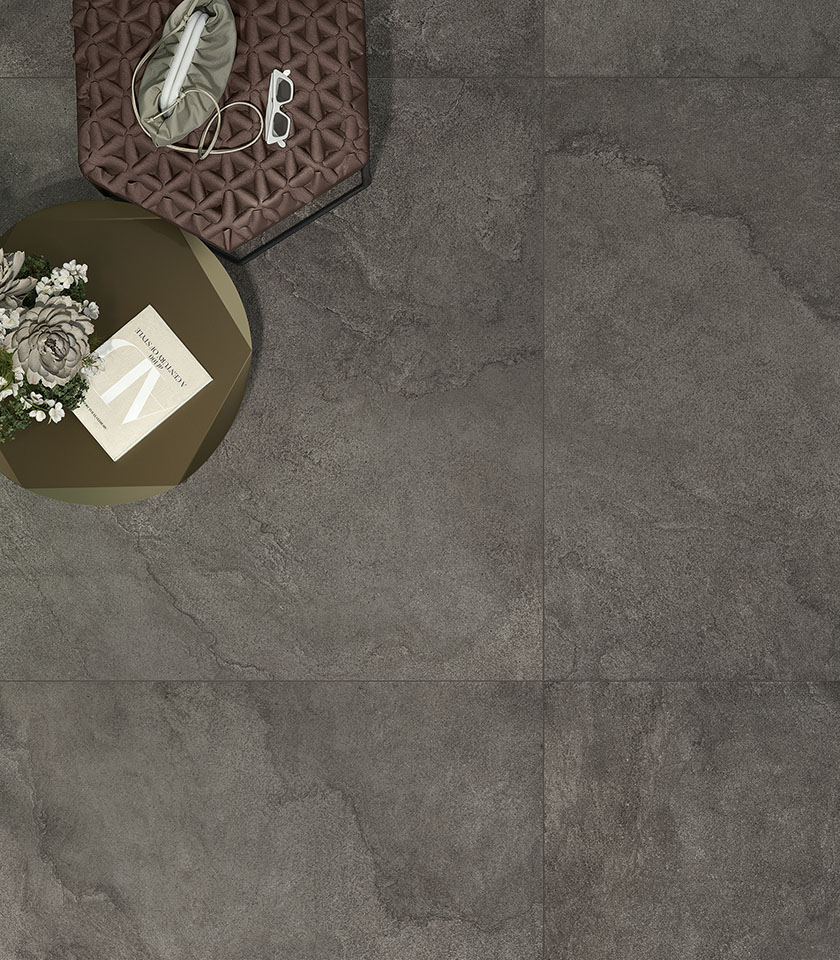 Pavimento in gres porcellanato effetto pietra scura in grande formato, con tavolini e dettagli decorativi contemporanei.