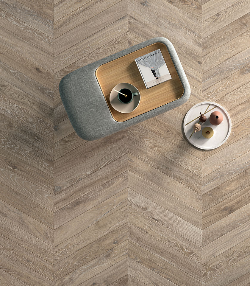 Pavimento in gres porcellanato effetto legno con posa a chevron, visto dall’alto con tavolini dal design contemporaneo.