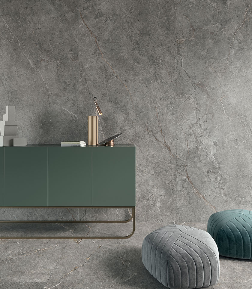 Pavimento in gres porcellanato effetto pietra scura in grande formato, visto dall’alto con tavolino, seduta e accessori decorativi.