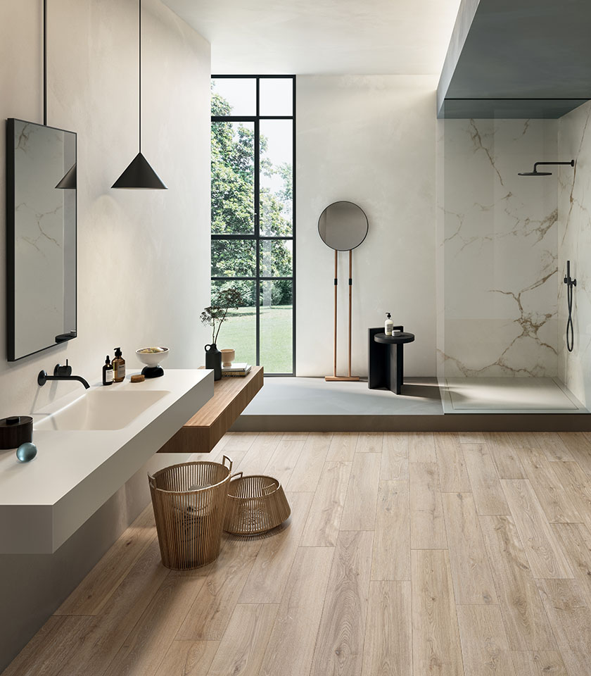 Bagno moderno e luminoso con pavimento effetto legno chiaro, superfici effetto marmo e arredi minimal per un’atmosfera elegante e naturale.